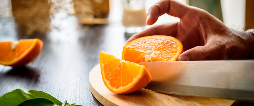 pessoa cortando uma laranja, uma das frutas mais ricas em vitamina c